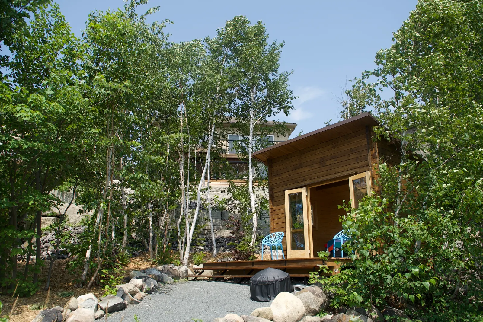 Cabin and main house set among birch trees, with a natural stone retaining wall at the base