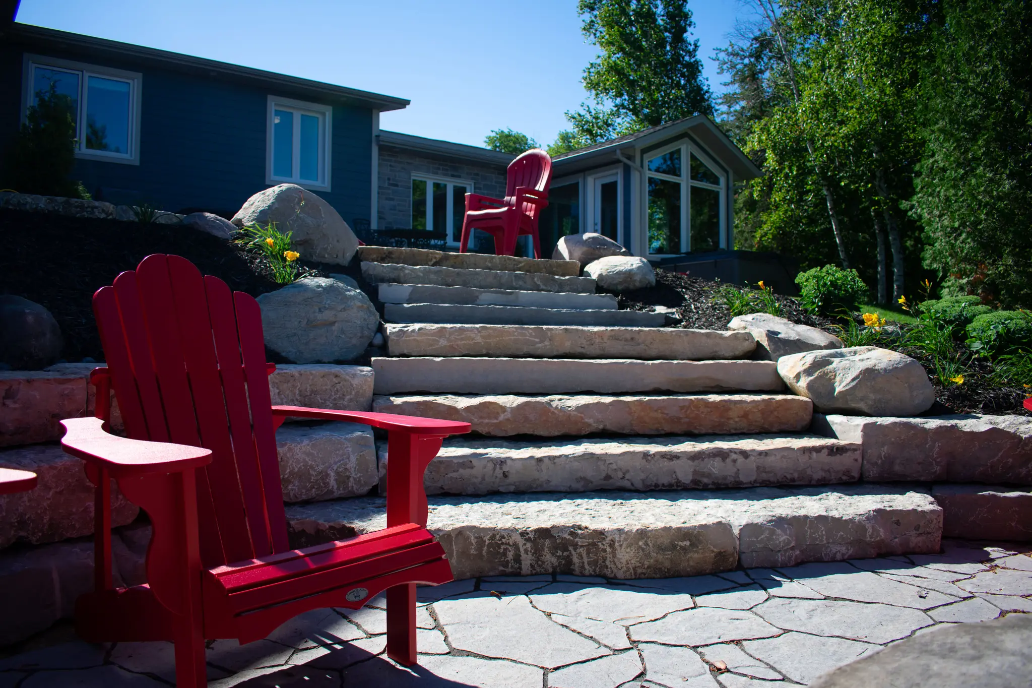 Boulder-flanked natural stone staircase leading up to a flagstone patio with red Adirondack chairs