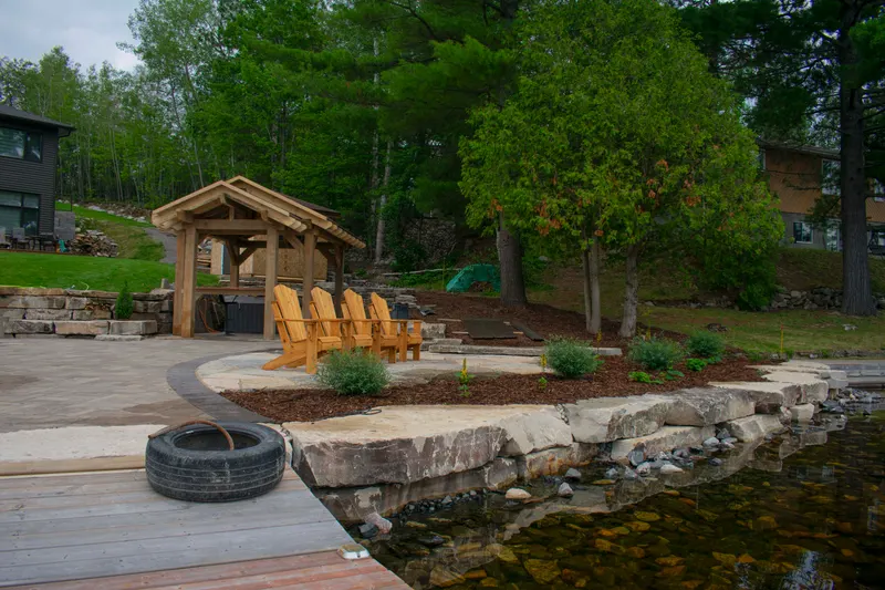 Wide view of the stone patio, pergola and fire pit area beside the lake