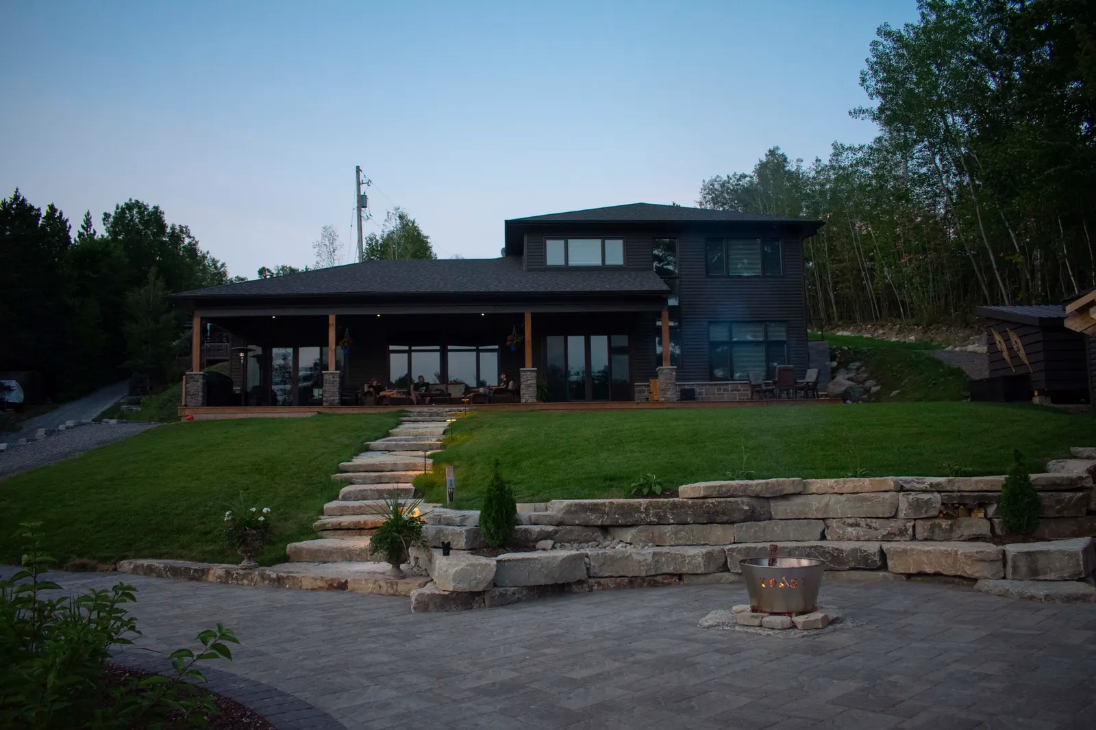 Wide dusk view of the lakefront house, stone entry steps and retaining wall